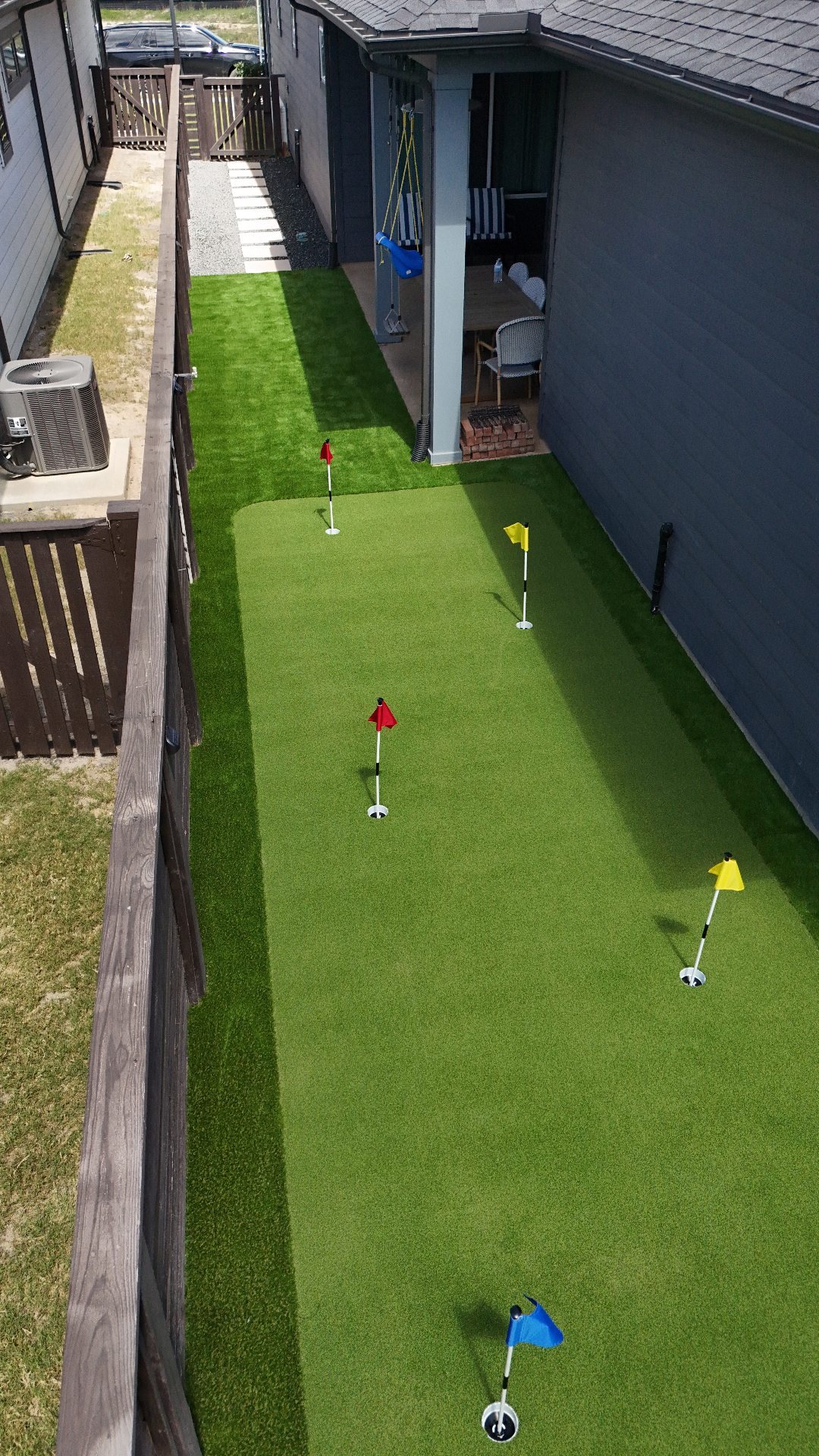Long narrow backyard putting green with multiple practice cups beside patio