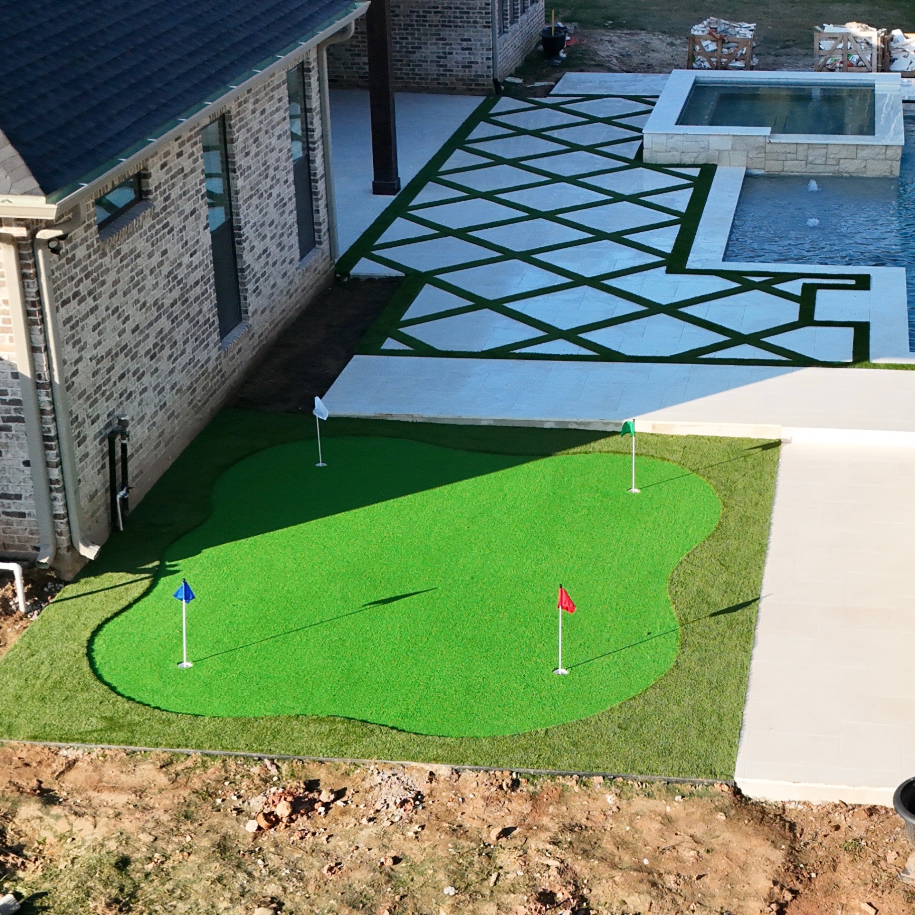 Backyard putting green with turf-and-paver geometric patio leading to pool and spa